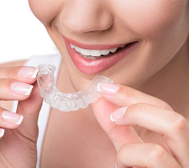 A clear Invisalign aligner held up in front of a smile