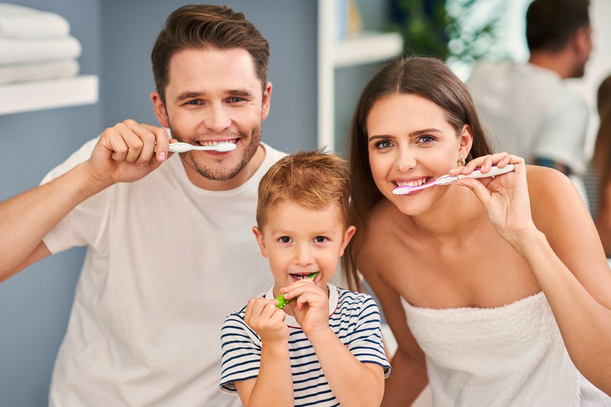 Parents and their young son brushing their teeth together at home