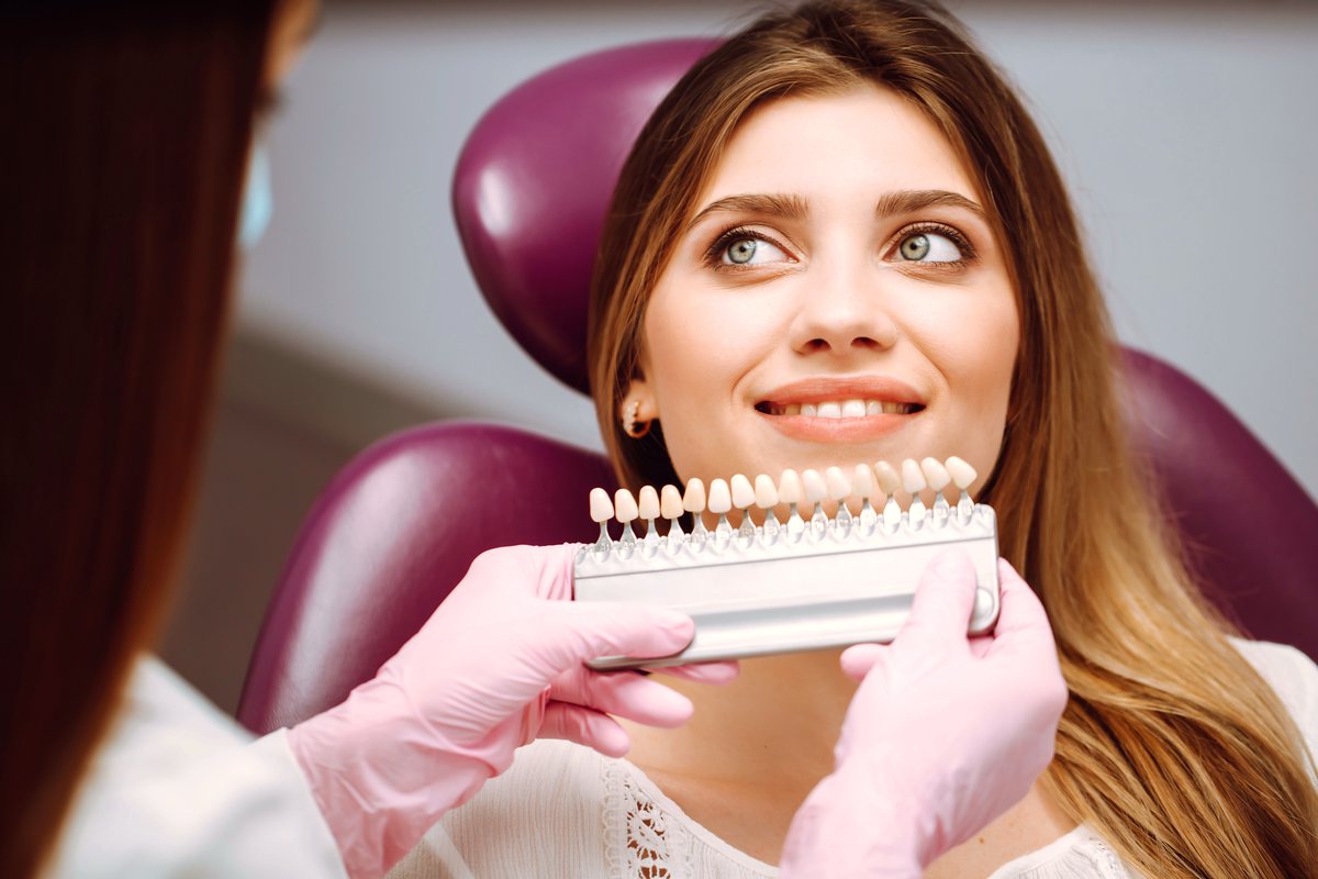 A tooth shade guide held up to a smiling patient in the dental chair